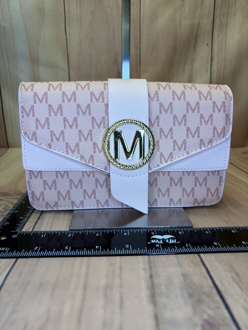 Soft pink monogram-style crossbody bag featuring an all-over “M” pattern